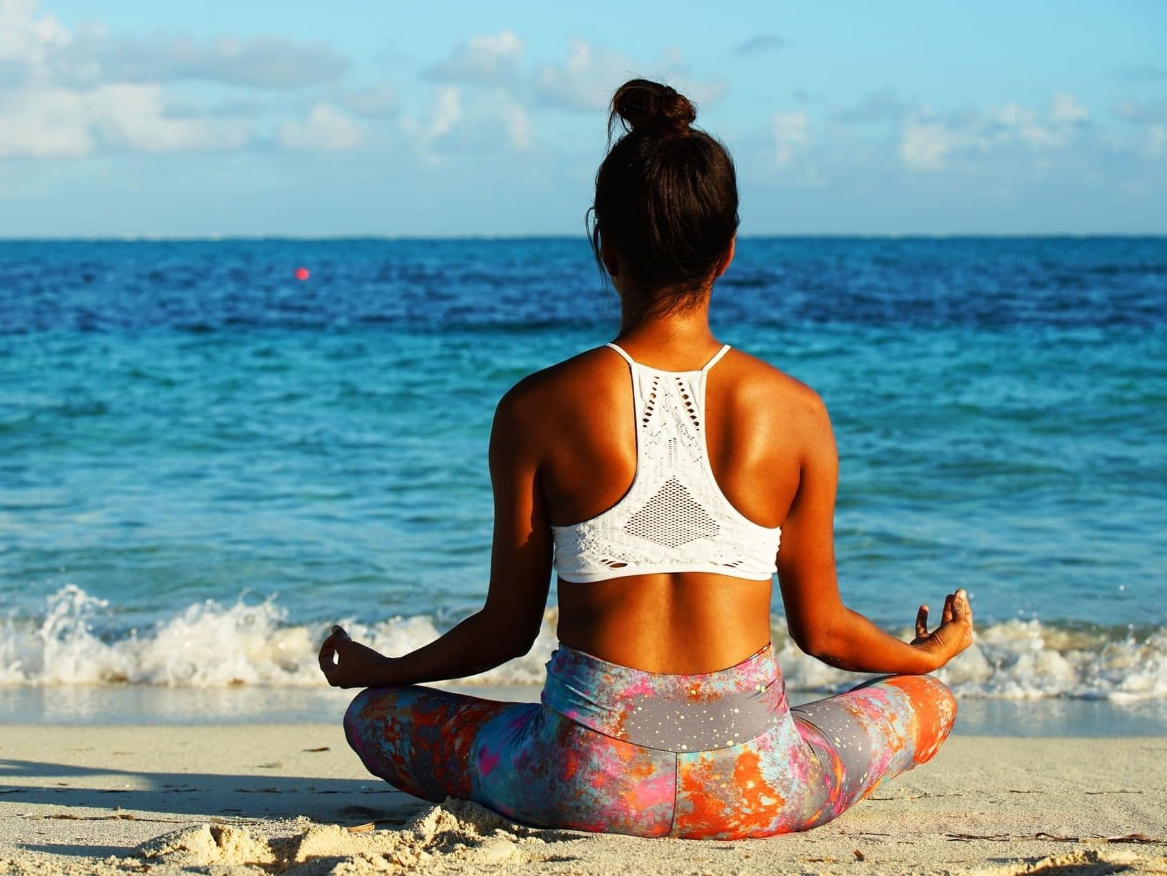 Woman meditating on a beach facing the ocean at sunrise
